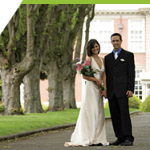 A young couple poses for wedding pictures on a formal garden lawn.